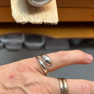 Anello serpente da mignolo in oro con dettagli intricati, firma Cécile Battistini, indossato sul dito mignolo.